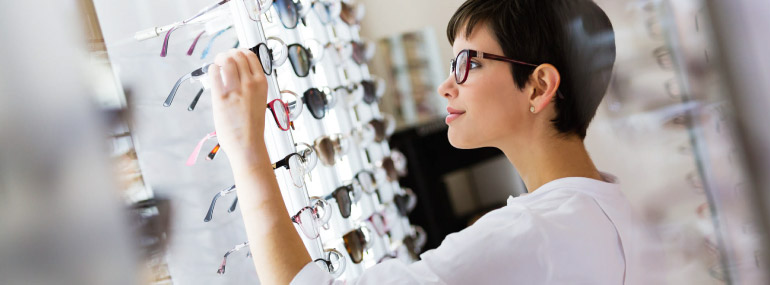 Woman looking through walls of eye glasses, searching for a new pair.