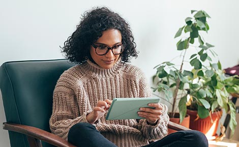 Woman using a tablet sitting in a chair near plants.