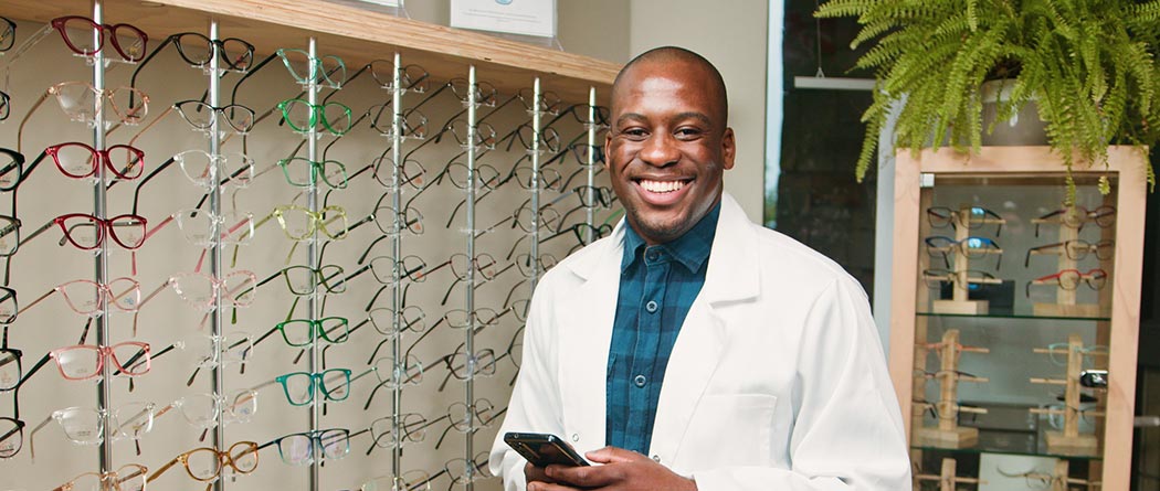 Doctor holding phone in front of glasses wall.