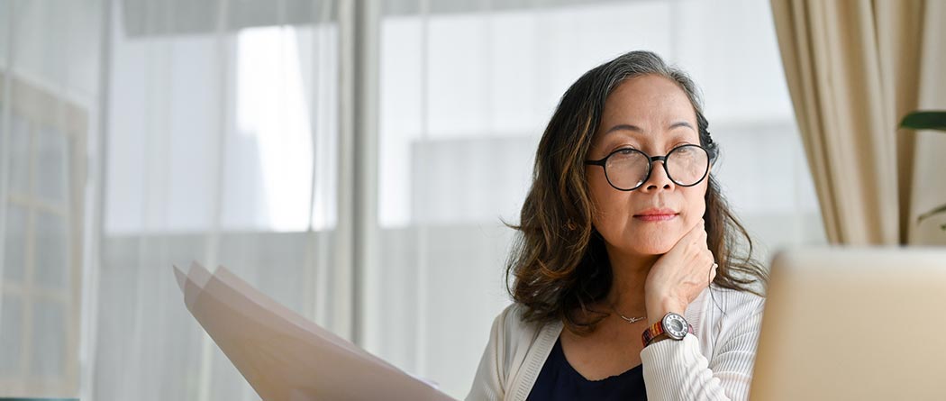 Woman looking at laptop while holding papers.